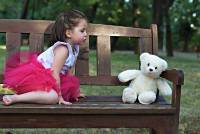 Meisje op een bank in het park met haar speelbeertje